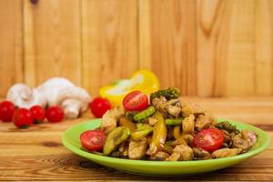 Stir fry chicken, zucchini and broccoli on wooden background photo