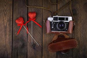 Vintage old camera with hearts on rustic wooden background. Top view