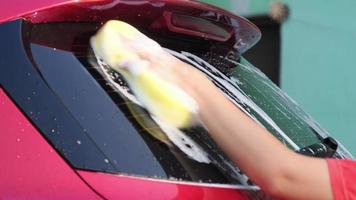 primo piano della mano di una donna che lava un'auto con spugna e sapone sull'autolavaggio. lavaggio auto manuale con sapone bianco. concetto di servizio di autolavaggio. video