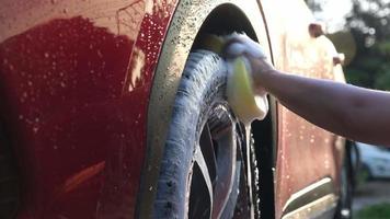 Nahaufnahme der Hand einer Frau, die ein Auto mit Schwamm und Seife auf der Autowaschanlage wäscht. manuelle autowäsche mit weißer seife. autowaschservice-konzept. video