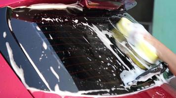 Close-up of a woman's hand washing a car with sponge and soap on the car wash. Manual car wash with white soap. Car wash service concept. video