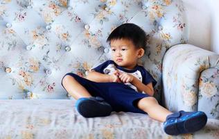Naughty asian boy sitting on light blue sofa in living room. photo