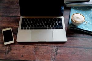 Laptop with smartphone and hot coffee on wooden table, Working remotely. photo