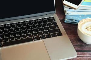 Laptop with a cup of hot coffee, smartphone and magazine on wooden table, Working remotely. photo