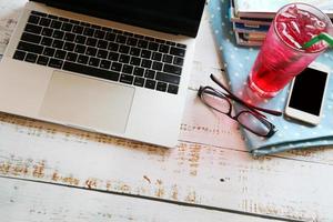 Laptop with glasses, smartphone, a glass of soft drink and books on wooden table, Working remotely. photo