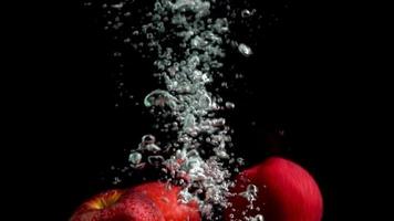 tres manzanas caen al agua y las burbujas de aire suben a la superficie del agua. video