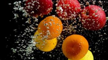 een verscheidenheid aan fruit valt in het water in een helder glazen aquarium en luchtbellen stijgen naar de oppervlakte van het water. video