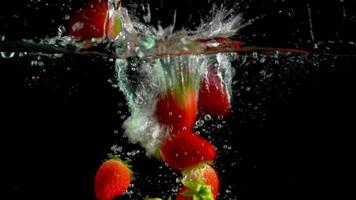 una varietà di fragole cade nell'acqua in un acquario di vetro trasparente e le bolle d'aria salgono sulla superficie dell'acqua. video