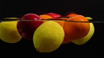 Slow motion many fruits floating on water and black background close up video