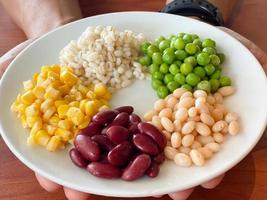 top view of navy bean and red bean and corn and  green peas and millet in white plate on hand photo