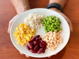 top view of navy bean and red bean and corn and  green peas and millet in white plate on hand photo