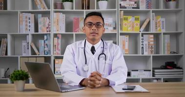 portrait d'un médecin de sexe masculin asiatique professionnel en blouse médicale blanche. lunettes d'homme faisant une conférence téléphonique et regardant la caméra. consultation patient à distance en ligne par webcam. notion de télémédecine.