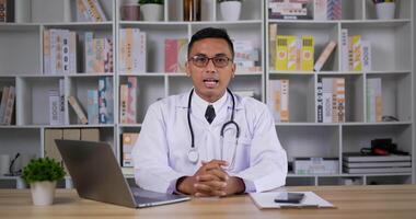 retrato de un médico asiático profesional con bata médica blanca. hombre haciendo una llamada de conferencia y mirando a la cámara. consultando al paciente a distancia en línea por cámara web. concepto de telemedicina. video