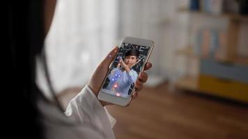 primer plano de una mujer viendo un teléfono inteligente en casa. mujer asiática demuestra el procedimiento correcto para usar una máscara transmitiendo video en vivo en pantalla móvil con emoji como y amor emocional.