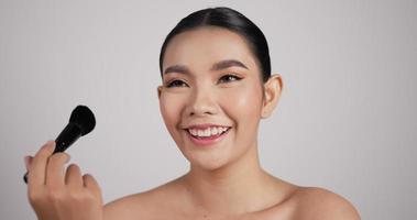 close-up de beleza mulher asiática faz make-up.beautiful modelo feminino faz blush no rosto usando pincel de maquiagem. conceito de anúncios cosméticos. video