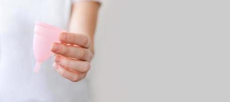 mano de mujer sosteniendo copa menstrual rosa aislada sobre fondo blanco. mujer alternativa moderna eco higiene ginecológica en el período de la menstruación. recipiente para sangre en la mano de una chica. foto