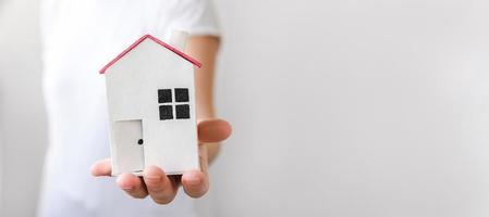 Woman hand holding toy model house isolated on white background. Real estate mortgage property insurance dream home concept. Offer of purchase rental house, family life, business real estate. photo