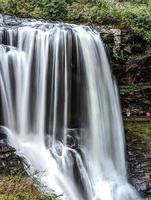 A scenic waterfall roadside going over the cliff down to the boulders and rocks below where you can no longer drive under but can walk underneath the raging waters photo