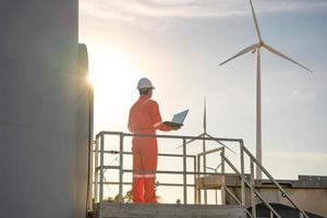 Man engineer working and holding the laptop for check performance of wind turbine farm Power Generator Station, Concept of sustainable resources, Concept of professional for the energy industry photo
