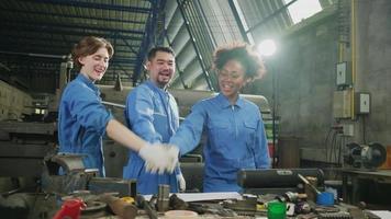 trabalhadores multirraciais da indústria em uniformes de segurança colaboram com unidade, dão as mãos e expressam um trabalho feliz junto com sorriso e alegria em uma fábrica mecânica, ocupação profissional de engenheiro.