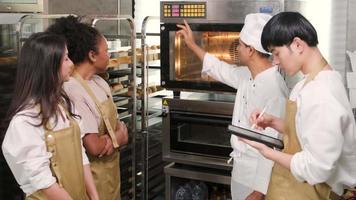 senior aziatische mannelijke chef-kok van culinaire leercursus leert en legt uit over elektrische oven aan kooklesstudenten voor het bakken van gebakdeeg voor brood en bakkerijproducten in roestvrijstalen keuken. video