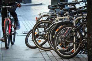 Bicycles stand in a row on a parking and one sportsman riding along the queue on a red bicycle photo