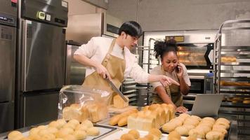 Two young friends and startup partners of bread dough and pastry foods busy with homemade baking jobs while cooking orders online, packing, and delivering on bakery shop, small business entrepreneur.