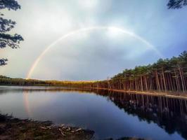 Lake after rain with a rainbow over it on a summer evening with forest reflection iin tranquil water
