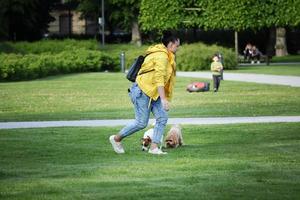 Vilnius, Lituania. 06 de junio de 2022 - mujer con chaqueta amarilla brillante jugando con dos perros pequeños en césped verde en el parque a principios de verano foto