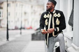 Mega stylish african man in traditional jacket pose. Fashionable black guy in hat. photo