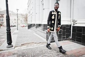 hombre africano mega elegante en pose de chaqueta tradicional. chico negro de moda con sombrero y gafas de sol con cigarro en la mano. foto