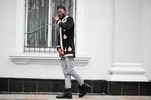 Mega stylish african man in traditional jacket pose. Fashionable black guy in hat and sunglasses with cigar in hand. photo