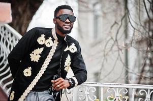 Mega stylish african man in traditional jacket pose. Fashionable black guy in sunglasses. photo