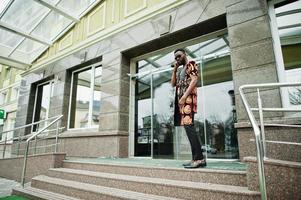 hombre elegante y guapo africano en traje tradicional y gafas de sol de pie al aire libre. foto