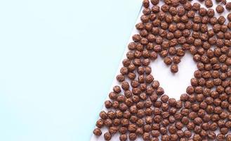 Background of chocolate cereal balls with copy space on blue and white papers. Heart shape from flakes. Dry breakfast cereal top view. Concept for a healthy diet. photo