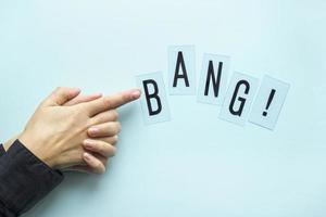 Female hand folded in sign of gun with BANG word. Close up consept on blue pastel background. Minimal flatlay style photo