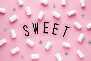 White marshmallows and stars with SWEET word on pink pastel background. Food concept in minimal flatlay style photo