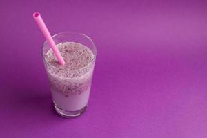 Glass of berry smoothie with straw on purple background. Pink milkshake with copy space. Healthy drink. Blueberry cocktail photo