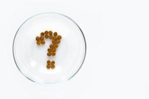 Question mark made of dry cat or dog food in bowl on white background. Concept of choosing a dry food for pet photo
