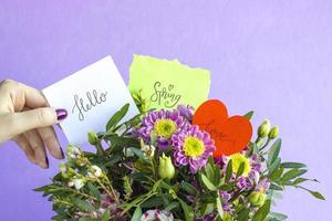 Floral composition with hand holding word HELLO, SPRING and LOVE on pink pastel background. Beautiful bouquet of spring flowers with copy space. Valentine Day, Mothers day, birthday, spring concept photo