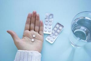 Woman hand holds two tablets with glass of water on  blured blue background. Health and medical concept treatment of diseases. Woman drinks tablets photo