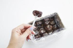 Female hand holds dried date palm fruits above box on white background. Pile of fresh date fruits for dietary nutrition. Top view photo