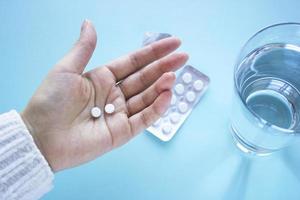 Woman hand holds two tablets with glass of water on  blured blue background. Health and medical concept treatment of diseases. Woman drinks tablets photo