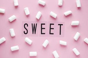 malvaviscos blancos y palabra dulce sobre fondo rosa pastel. concepto de comida en estilo flatlay mínimo foto
