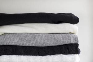 Close-up stack of folded monochrome clothes on white background wall. Black, grey and white textiles clothing. Horizontal view photo