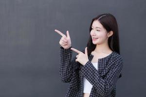 Asian professional working woman who wears black suit with braces on teeth is pointing hand to present something on the dark gray wall. photo