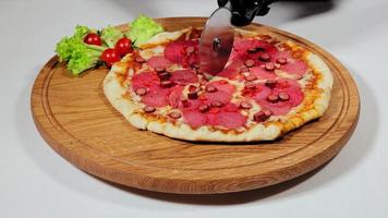 cortando pizza em triângulos com roda de cortador de pizza na tábua de madeira. close-up vista da mão humana na luva preta, separando a fatia de pizza na mesa branca. conceito de comida