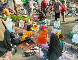 Sukoharjo - June 2, 2022 - an old man with a disability supervises and directs small children to color the painting photo