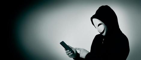 Anonymous hacker and face mask with smartphone in hand. photo