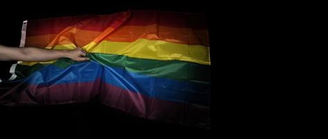 LGBTQ pride flag on black background. Lgbt rainbow flag in gay hand. photo